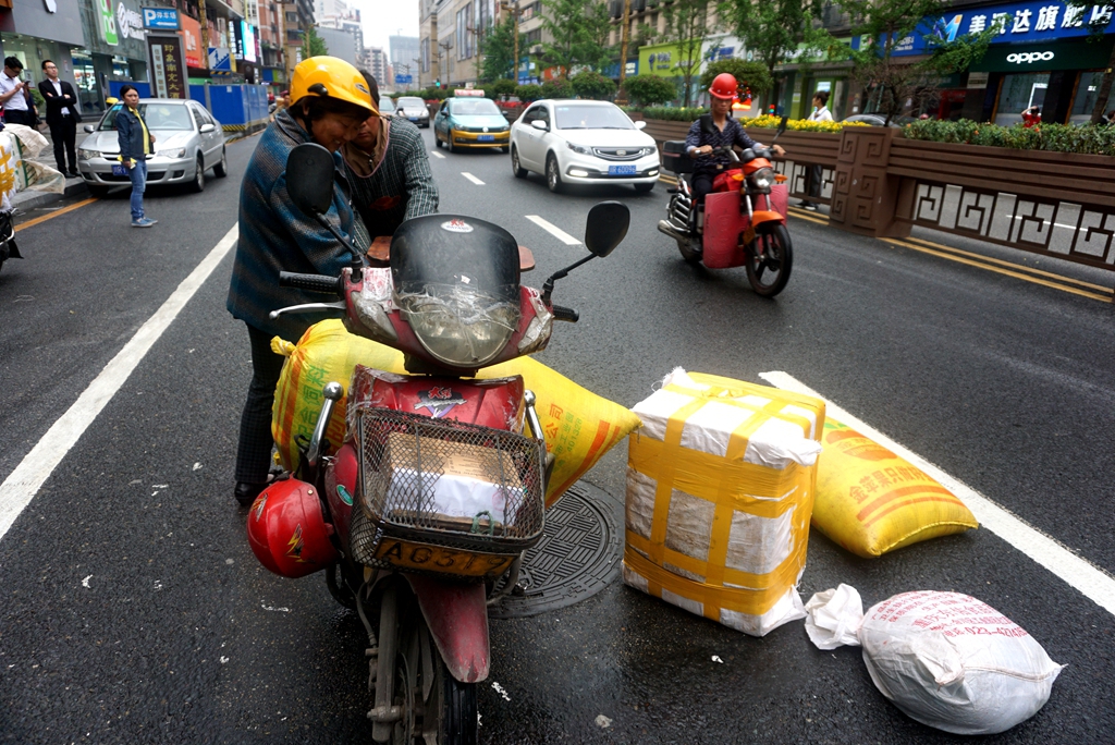 超载不可取,后果严重:人,车,货三倒地,拦了一大片,后面车辆受阻!